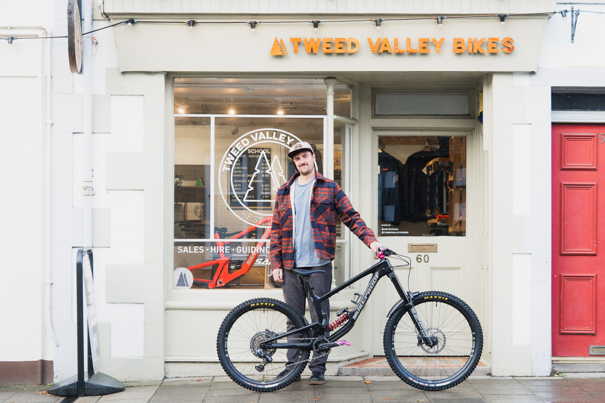 Tomy standing with his Nukeproof Giga RS 297 in front of Tweed Valley Bikes in Innerletihen